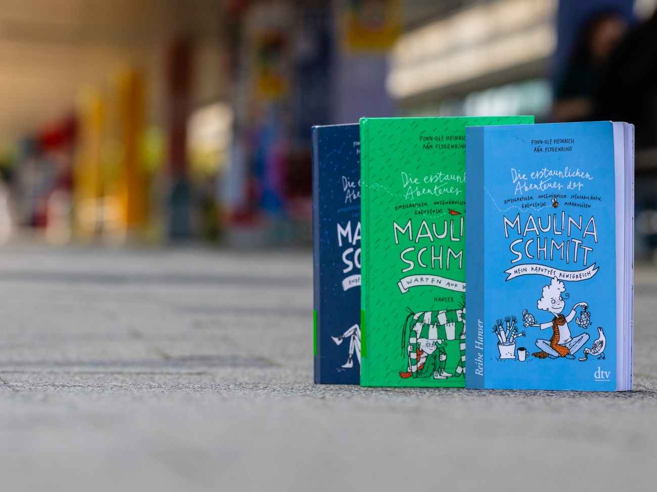 Drei Bücher stehen hintereinander aufgefächert auf dem Boden.