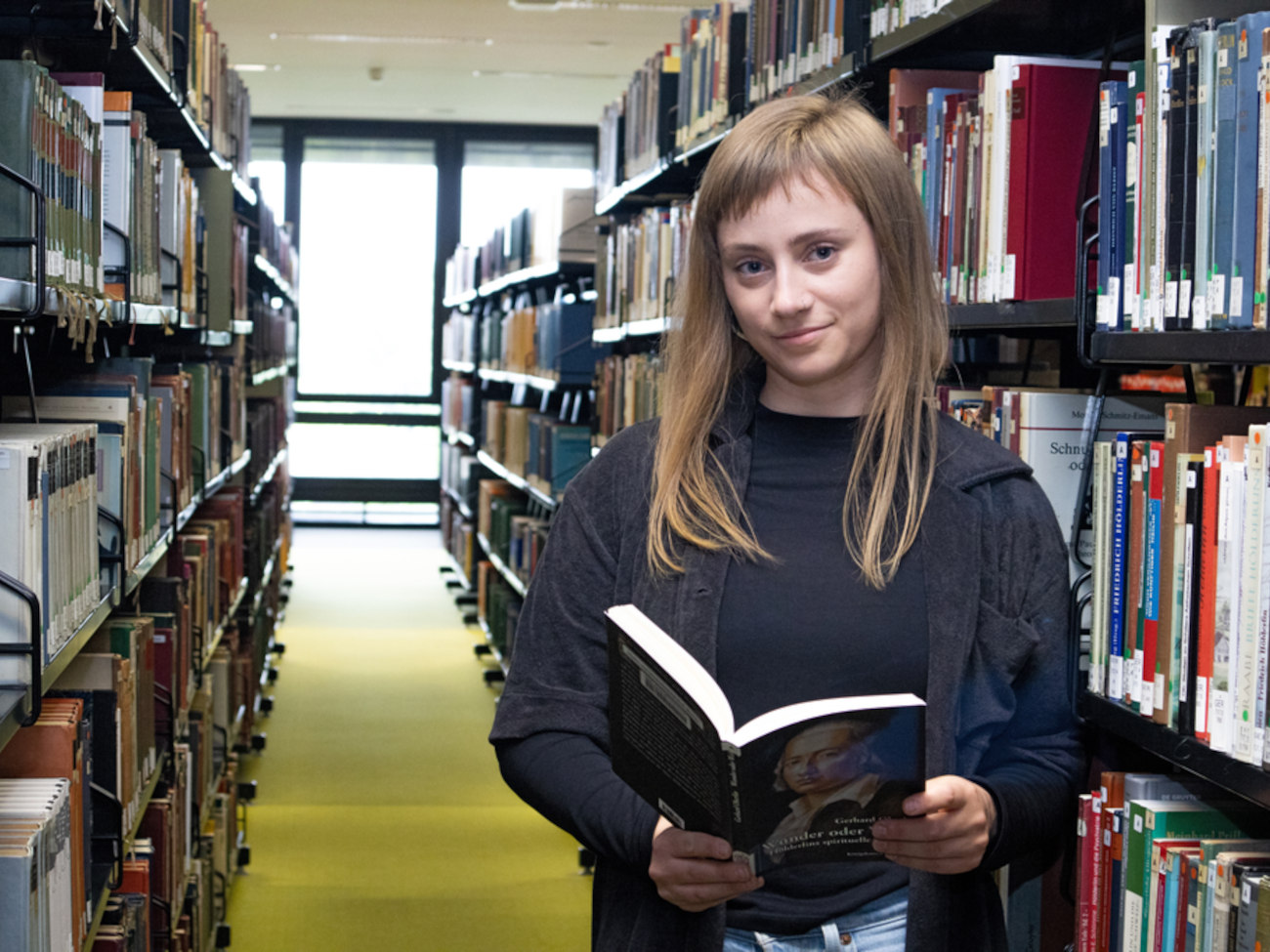 Jenny is holding a book in her hands while standing in the library.