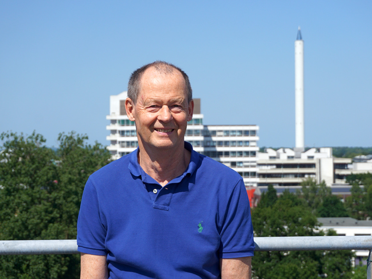 Dr. Justus Notholt stands on the rooftop terrace of NW1 Building. In the background, you can see the university campus with its Drop Tower.