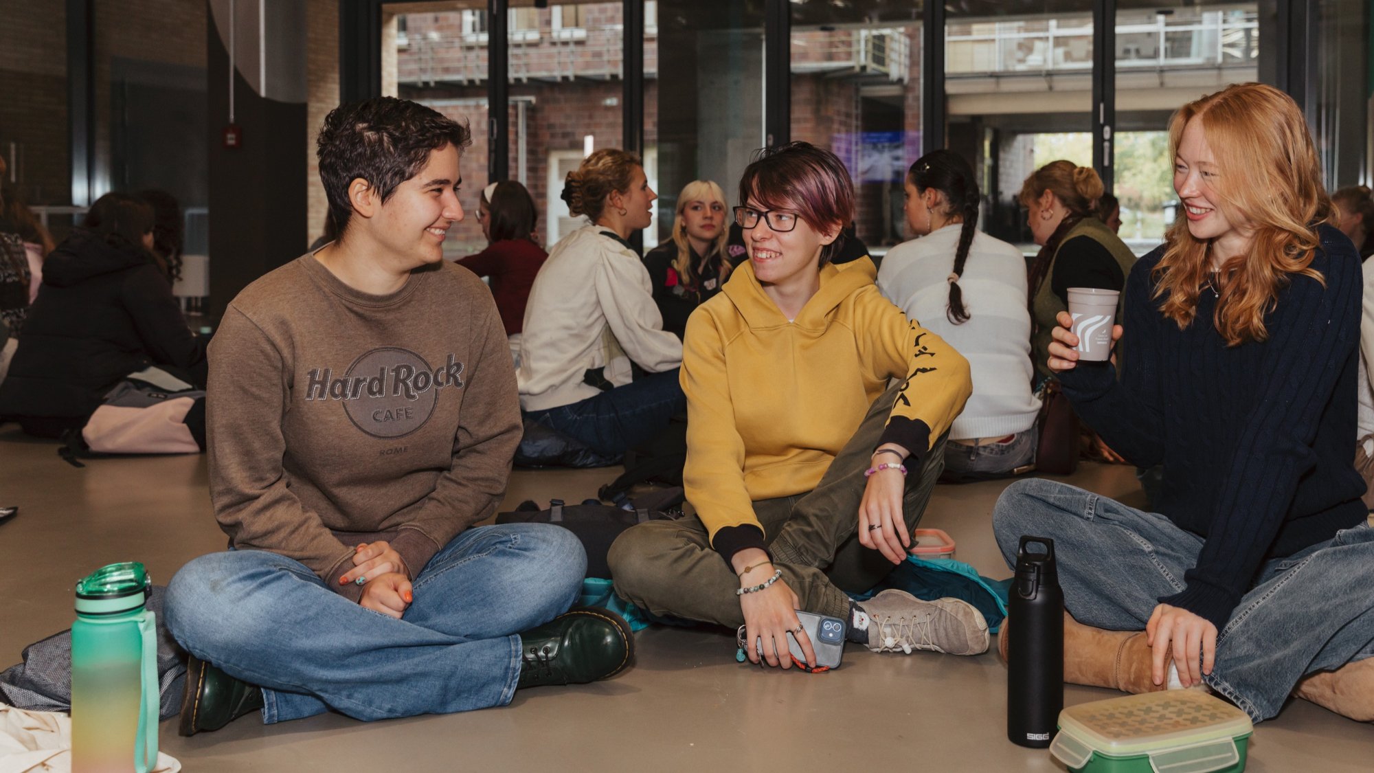 Drei Studierende sitzen auf den Boden und lachen zusammen.