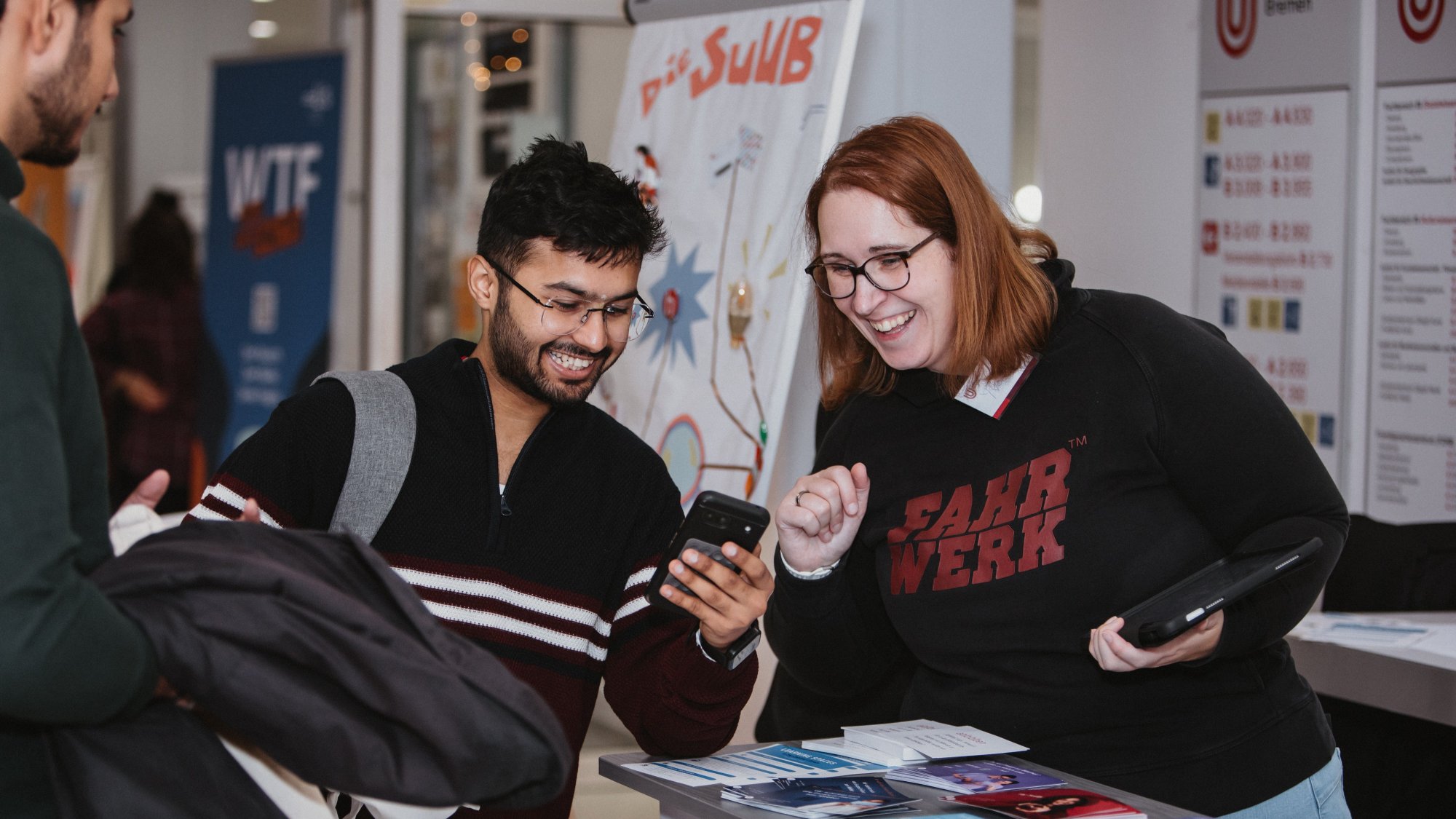 Zwei Personen an einem Infostand blicken auf ein Handy.