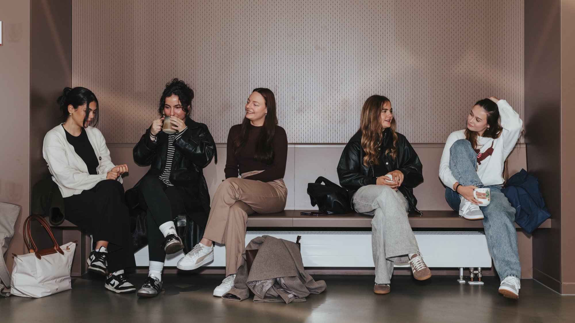 Fünf Personen sitzen auf einem Sofa an der Wand und unterhalten sich.