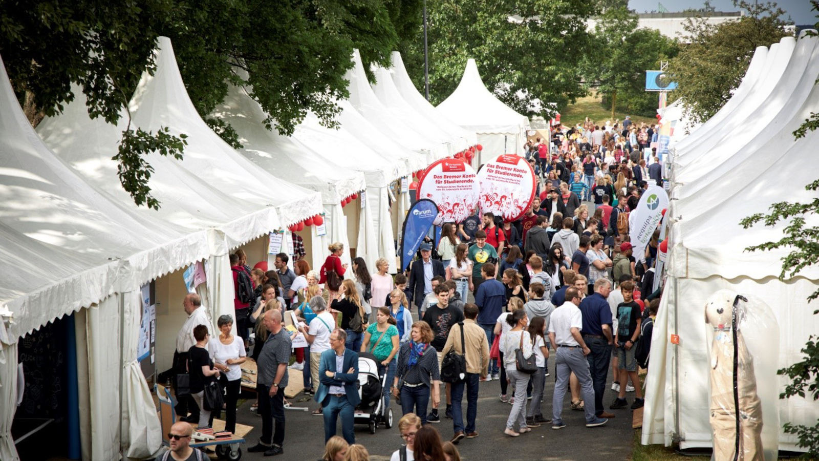 Menschen spazieren durch eine mit weißen Pagoden gesäumte Straße.