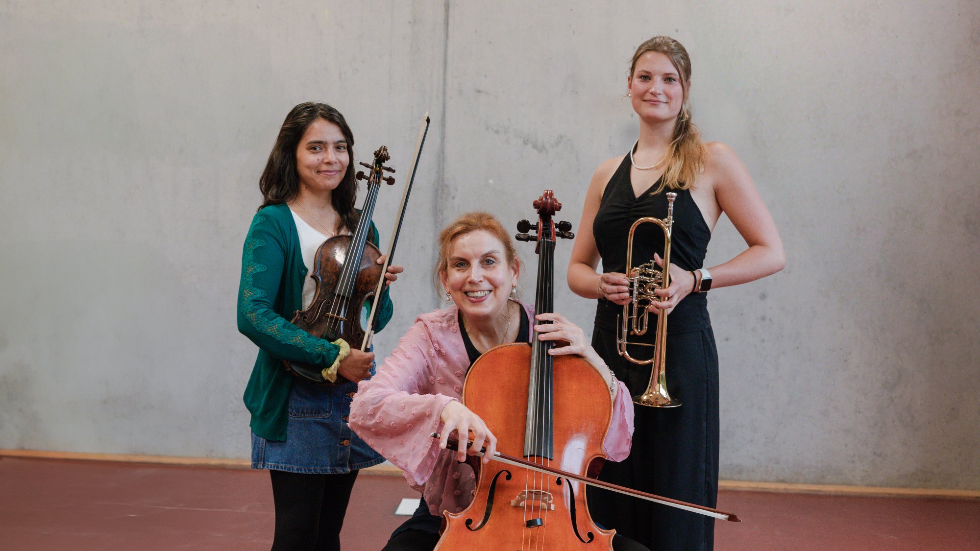 Three women with musical instruments are smiling at the camera. 