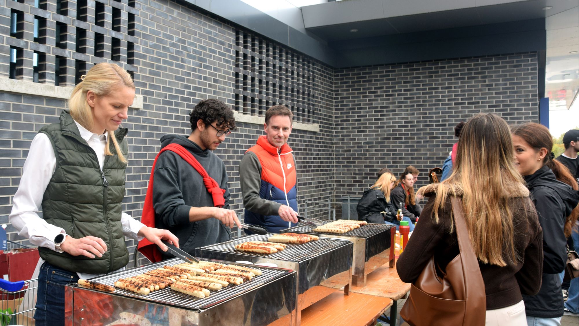 Drei Personen stehen hinter den Grills und wenden Grillgut.