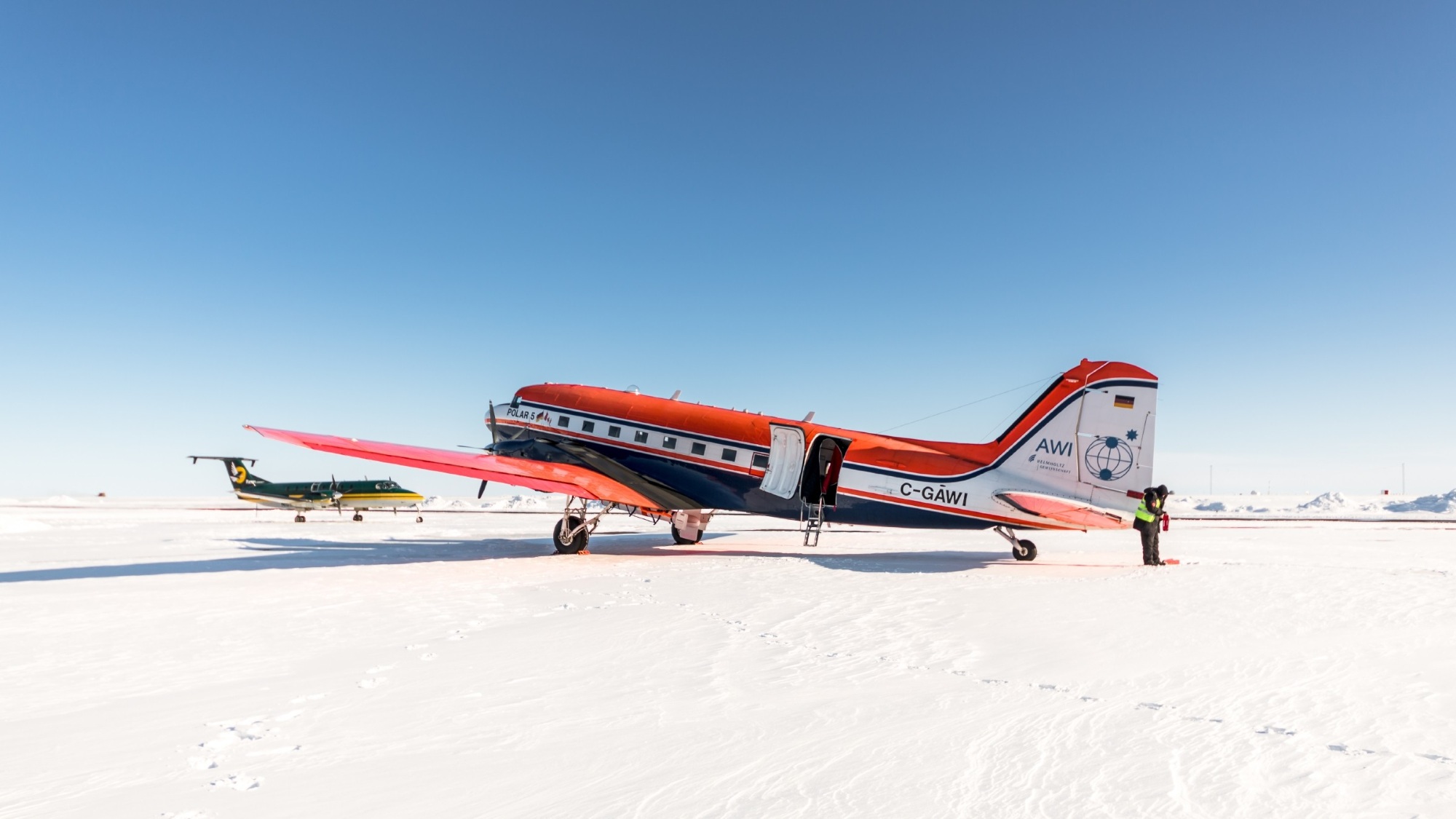 A red plane stands on a wide snowy field.