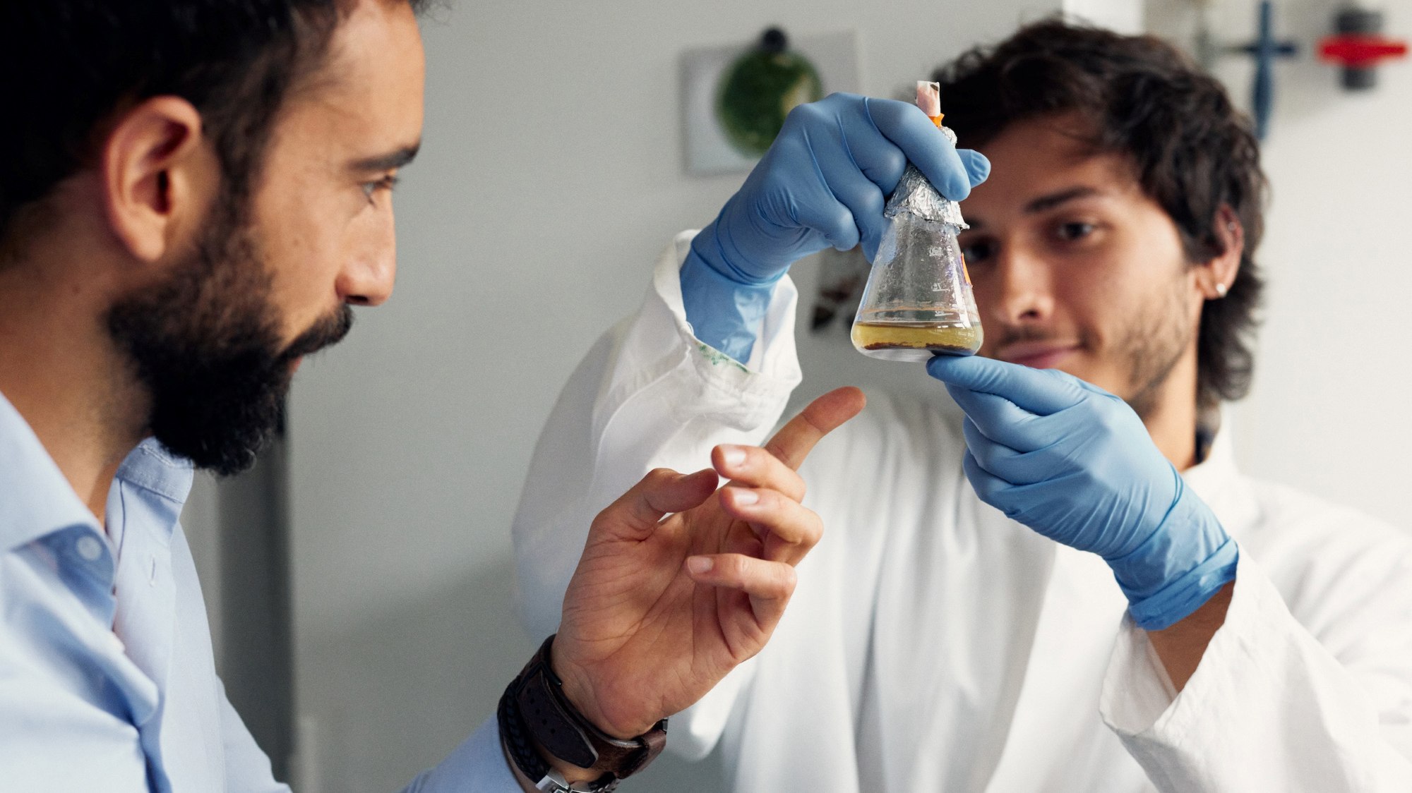 Two people in a laboratory examine a flask with liquid.