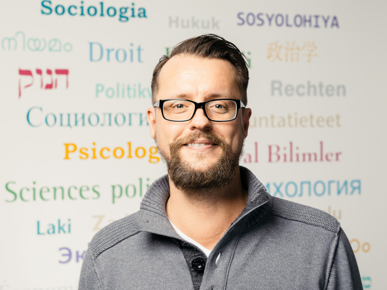 Christian Peters stands in front of a wall with colorful lettering from the social sciences in different languages.