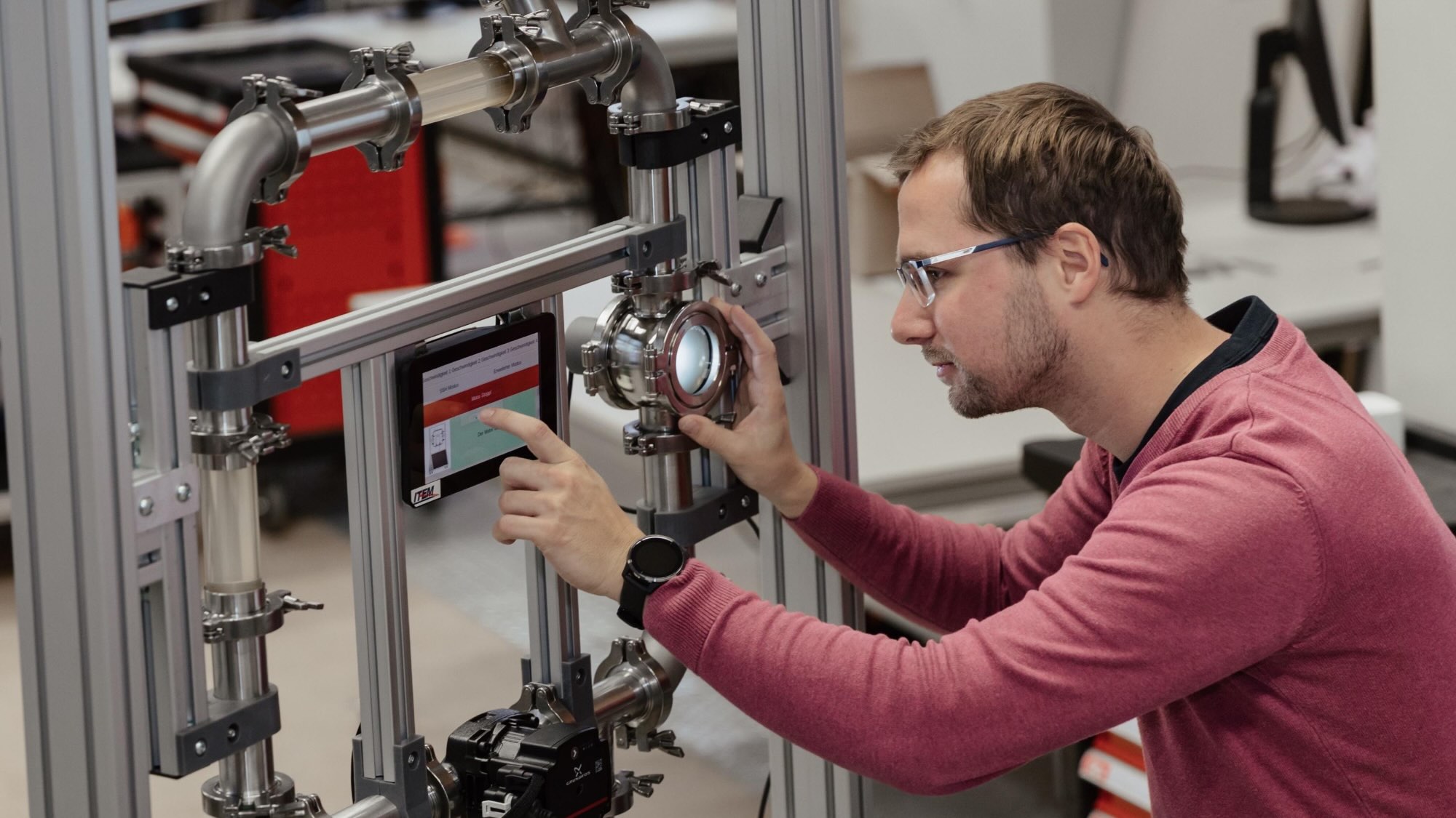 Eine Person hantiert mit einem Gerüst aus Rohren, die mit einem kleinen Bildschirm versehen sind.