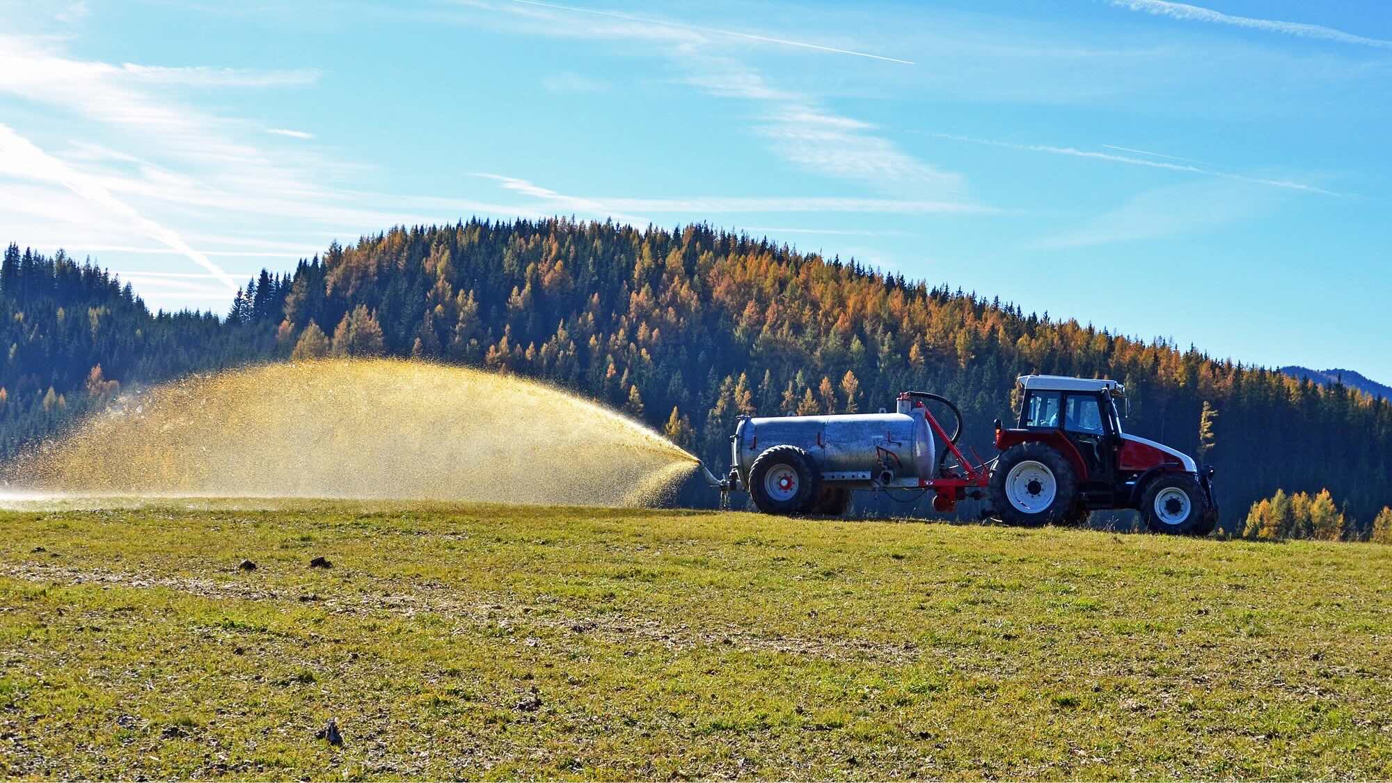 Ein roter Traktor düngt ein großes Feld.