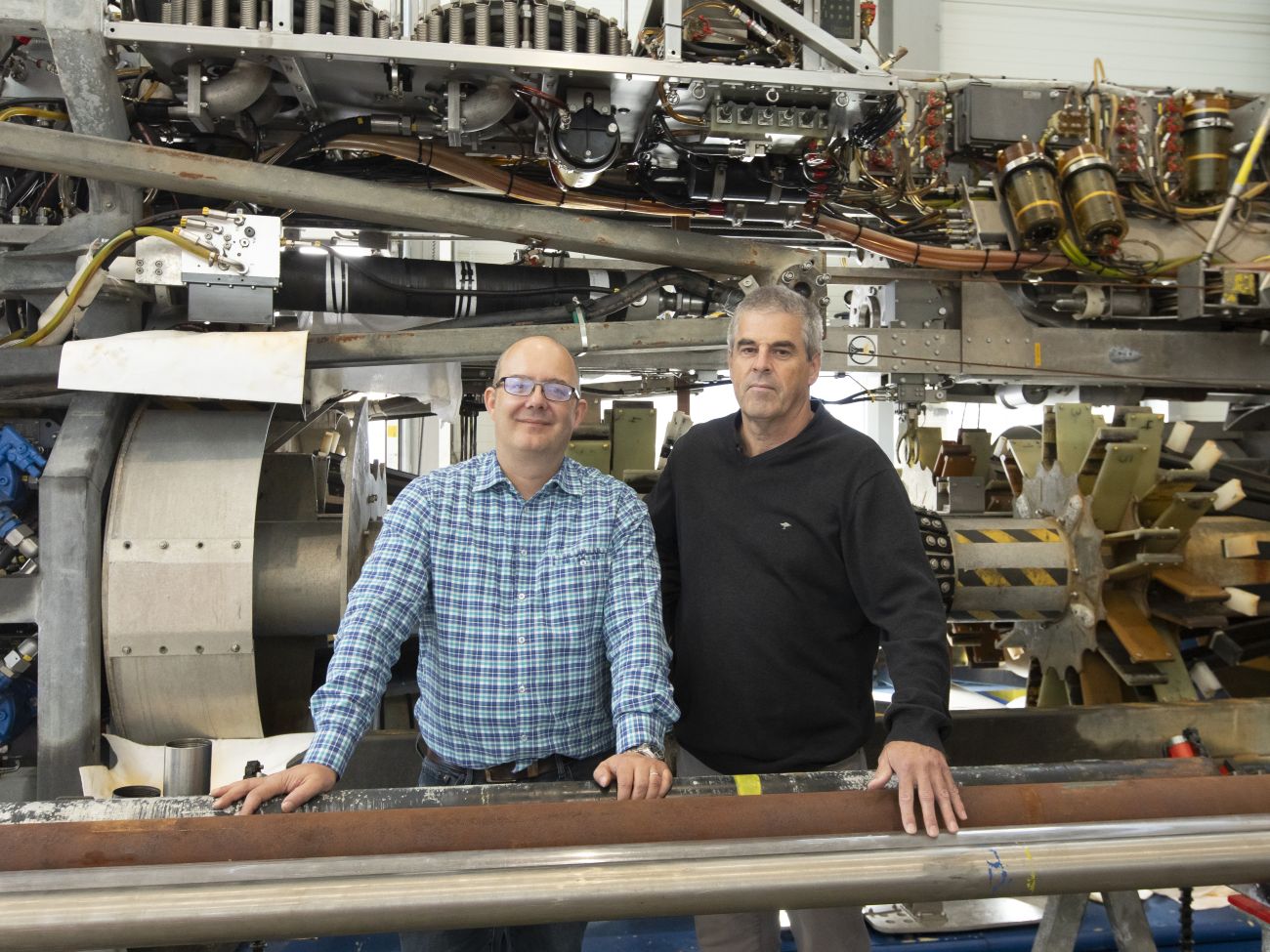 Two men standing in front of a huge machine. 