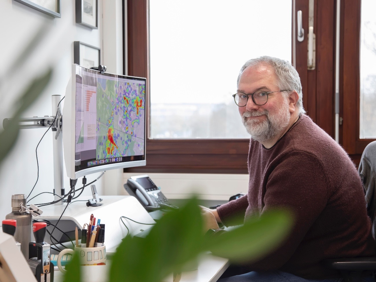 Professor Doktor Benjamin Schüz sitzt seitlich zur Kamera vor seinem Computer und lächelt in die Kamera.