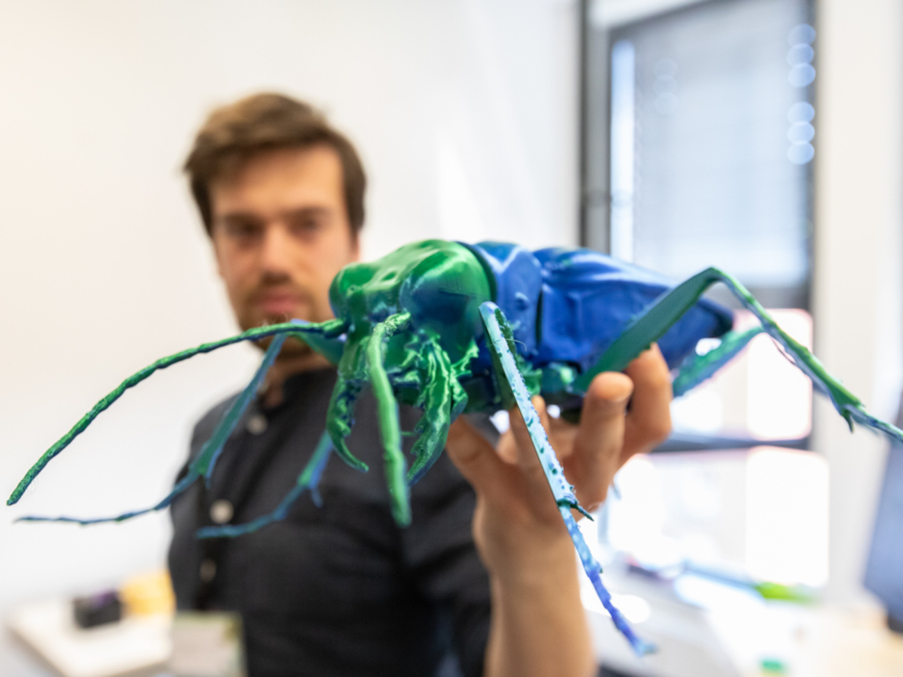 A man holding a 3D model of an insect up to the camera