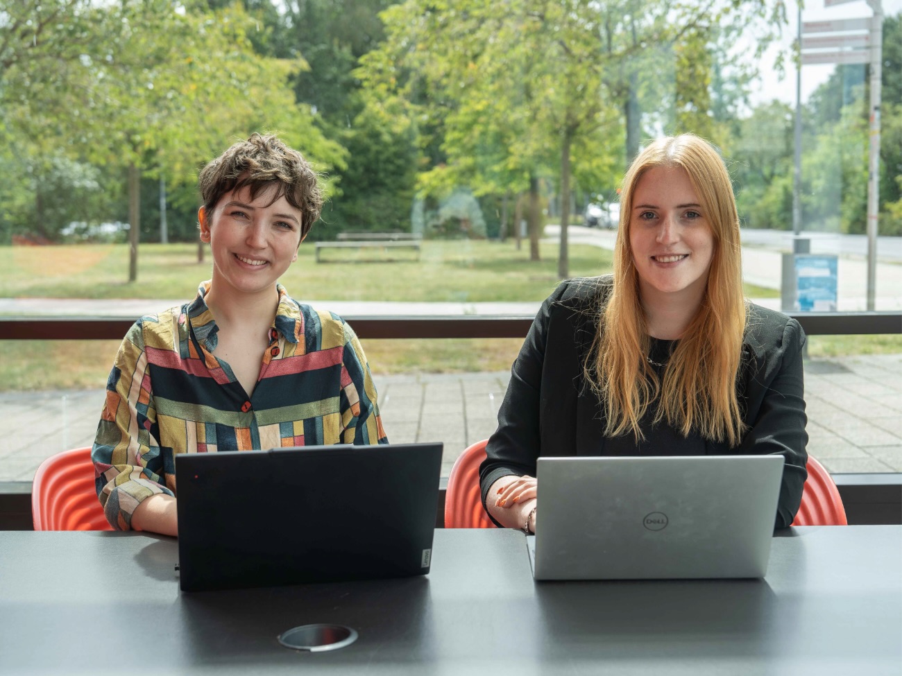 Caroline Dominik and Nicola Thoben are each sitting in front of a laptop and smiling at the camera.