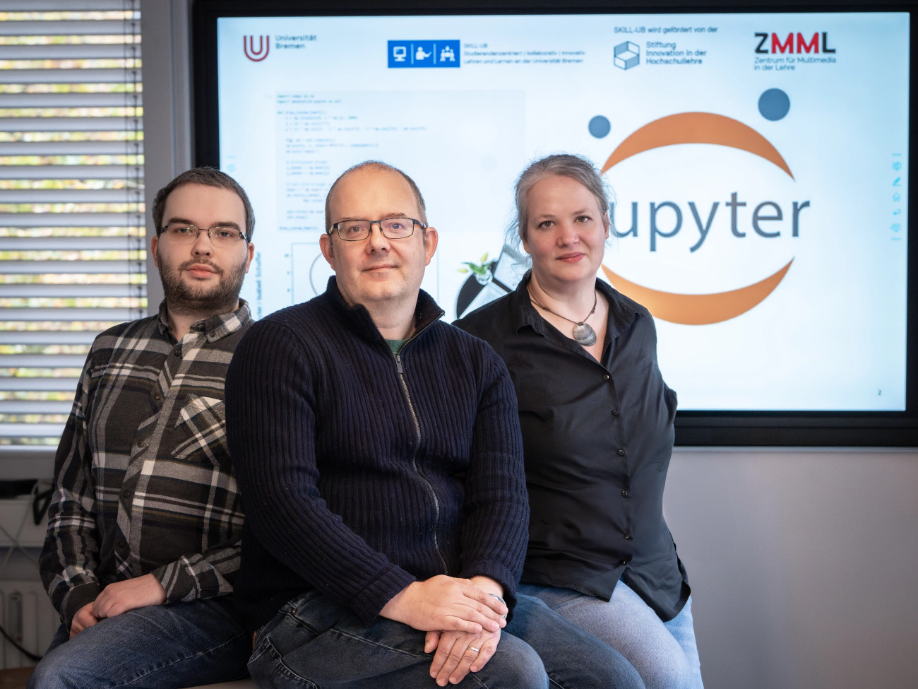 Isabell Schaffer, Marcel Meissner and Heiko Pälike sit at a table, with a JupyterHub presentation in the background.