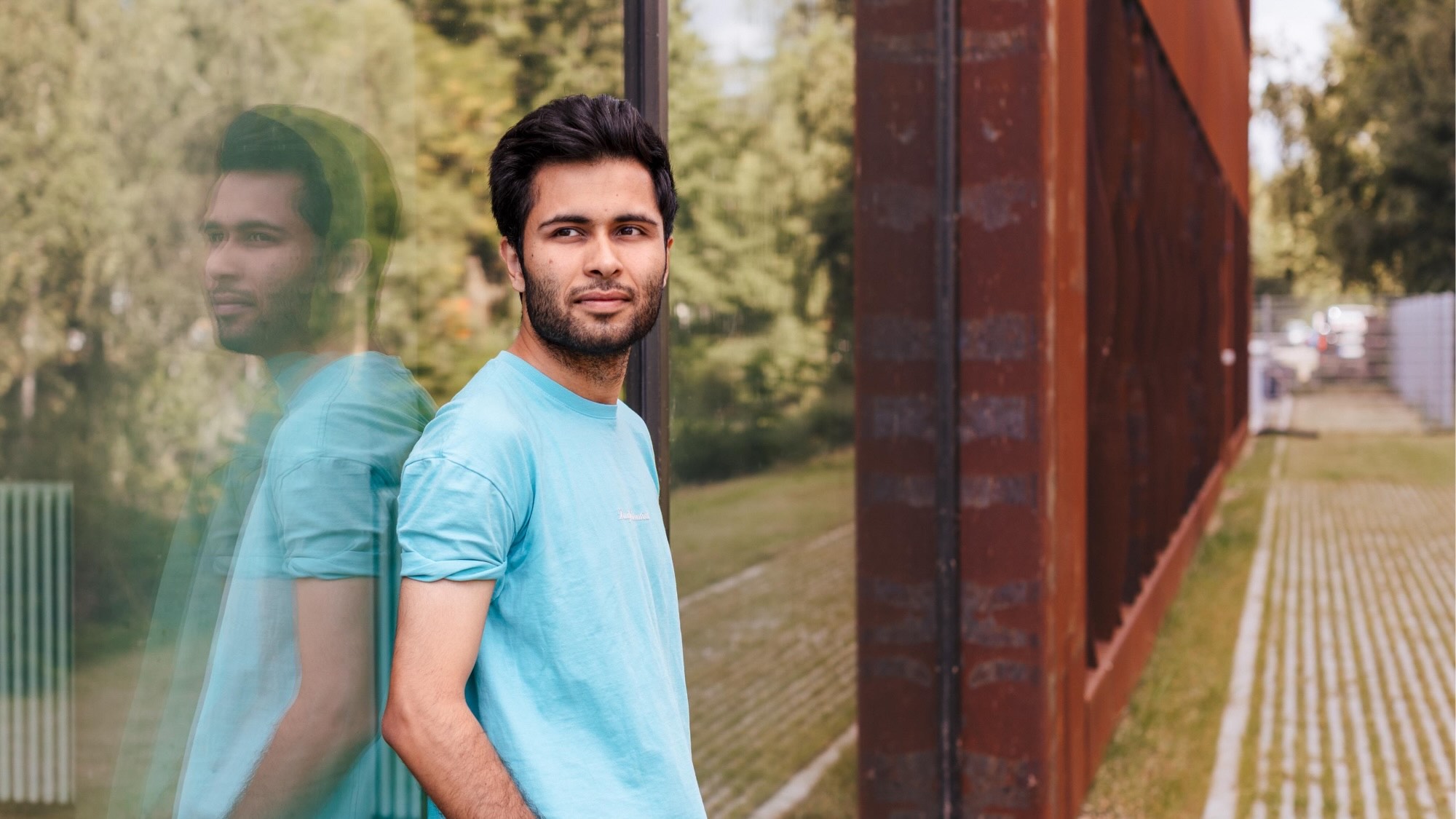 Muhammed Ahmed leans against a glass building and gazes into the distance. 