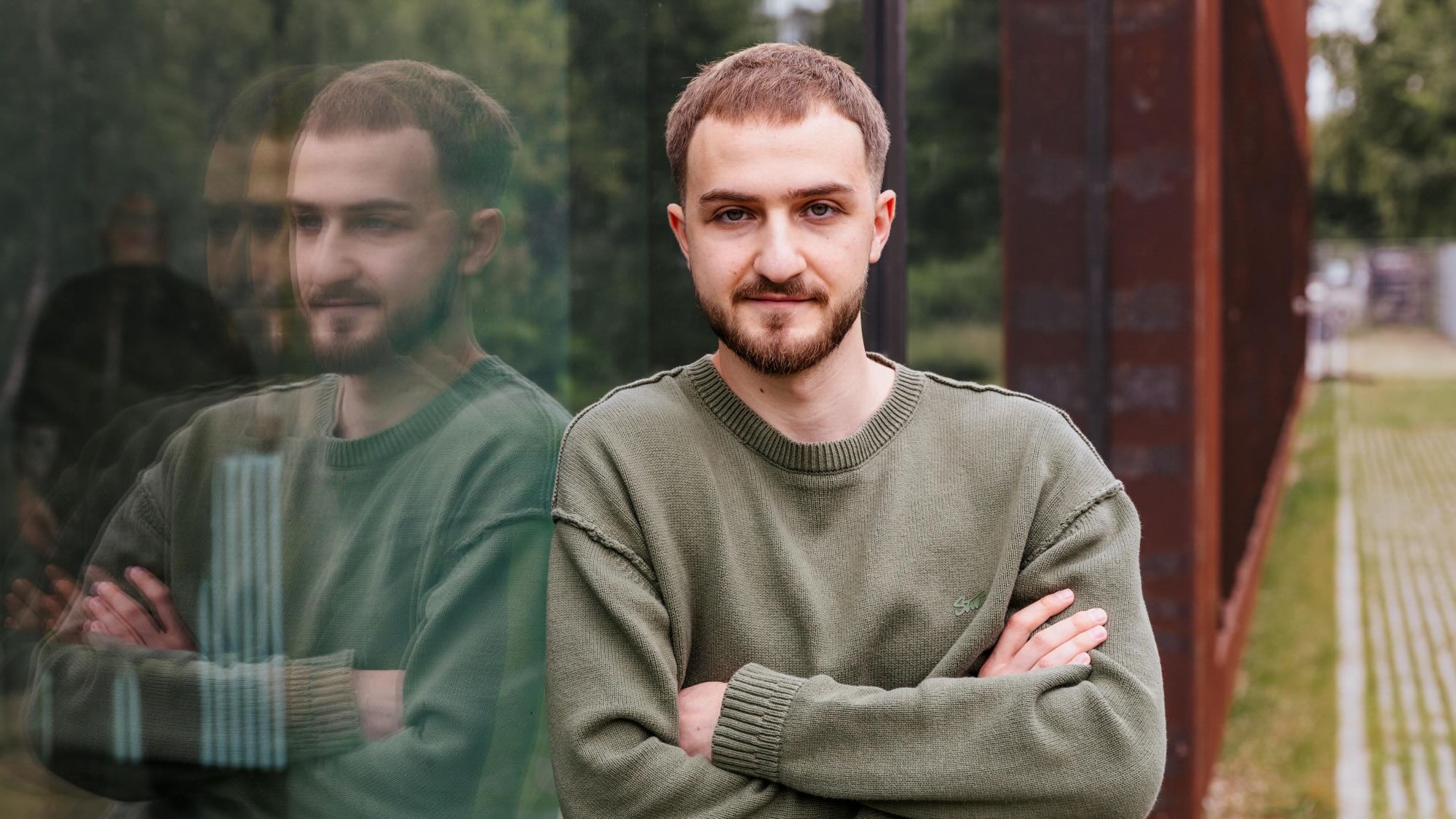 Dan is leaning against a glass window and smiling at the camera. 