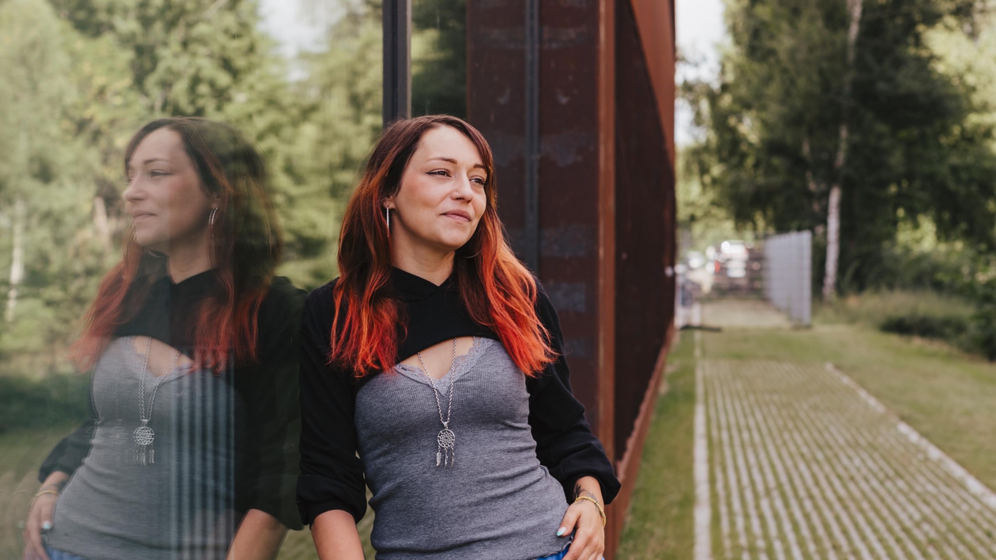 Jasmin Lanz is leaning against a glass building and gazing into the distance.