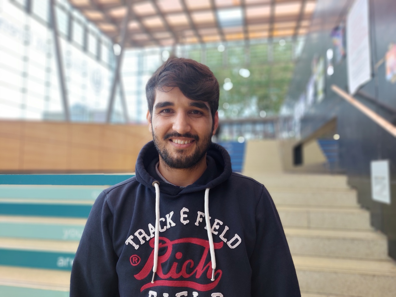 A man is standing in the glass hall and is smiling at the camera.