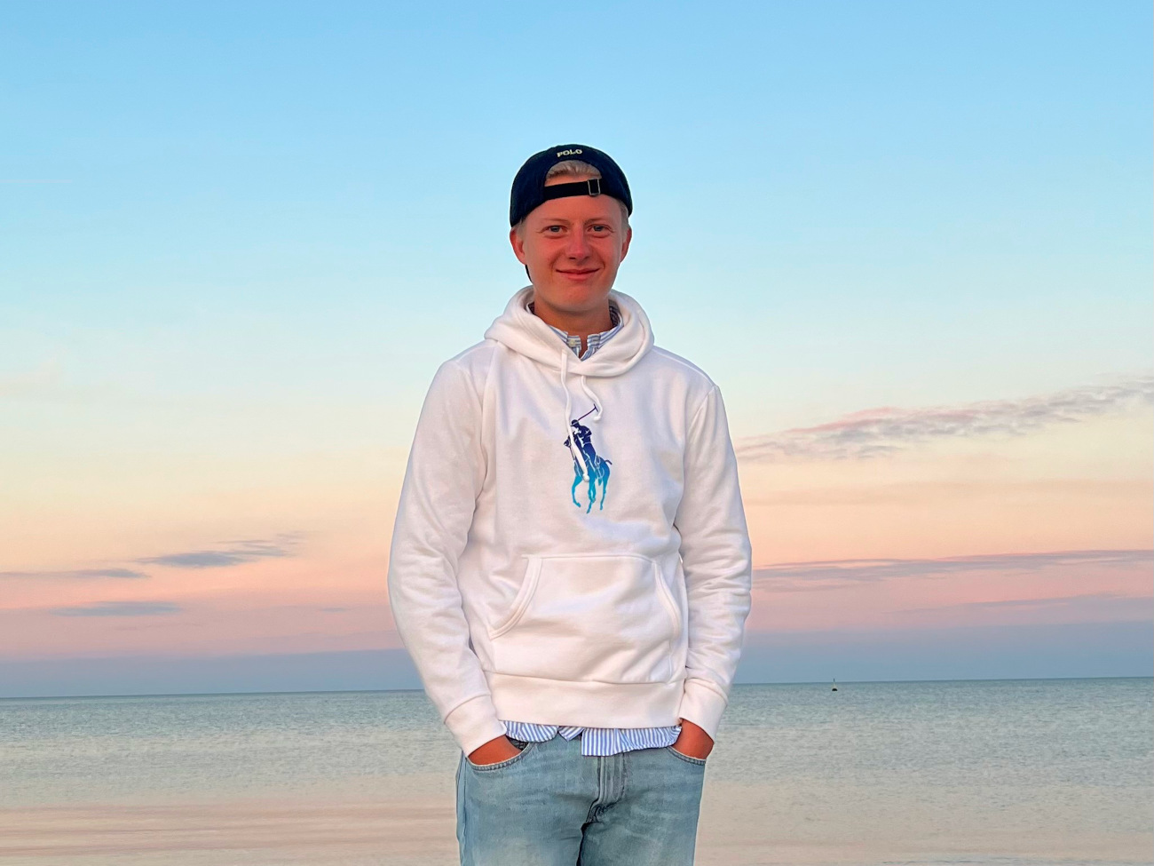 Rafael Ditter stands on the beach, with the sea and a sunset behind him.