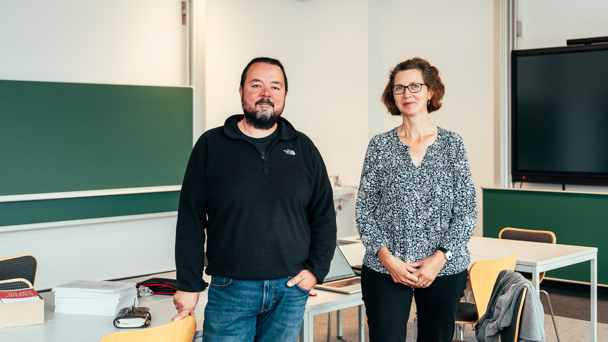 Professor Callies und Professorin Knipping stehen im Didaktiklabor vor dem Lehrerpult, im Hintergrund sind grüne Schultafeln zu sehen.