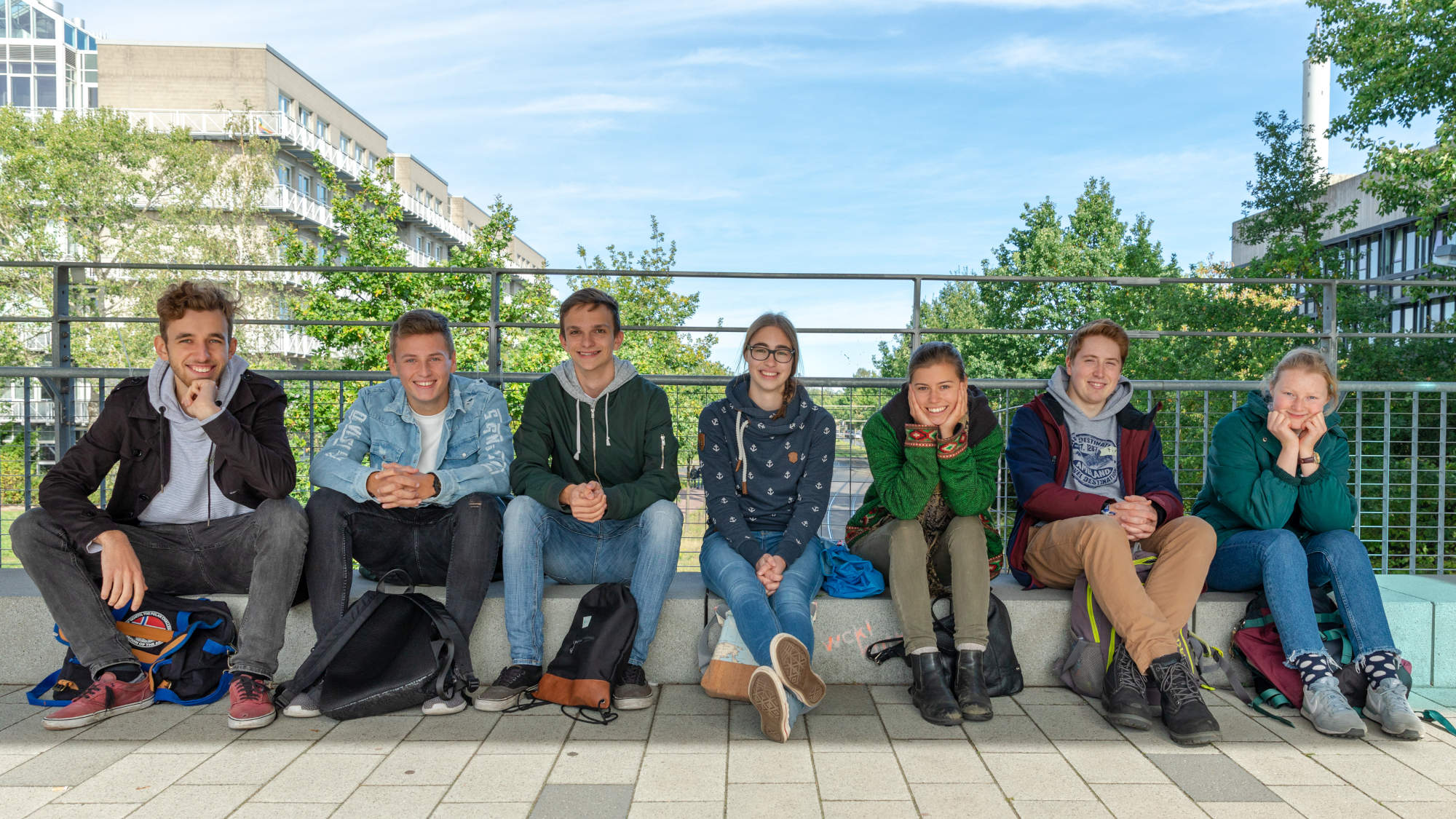 Seven first-year students sitting on the boulevard and smile into the camera. 