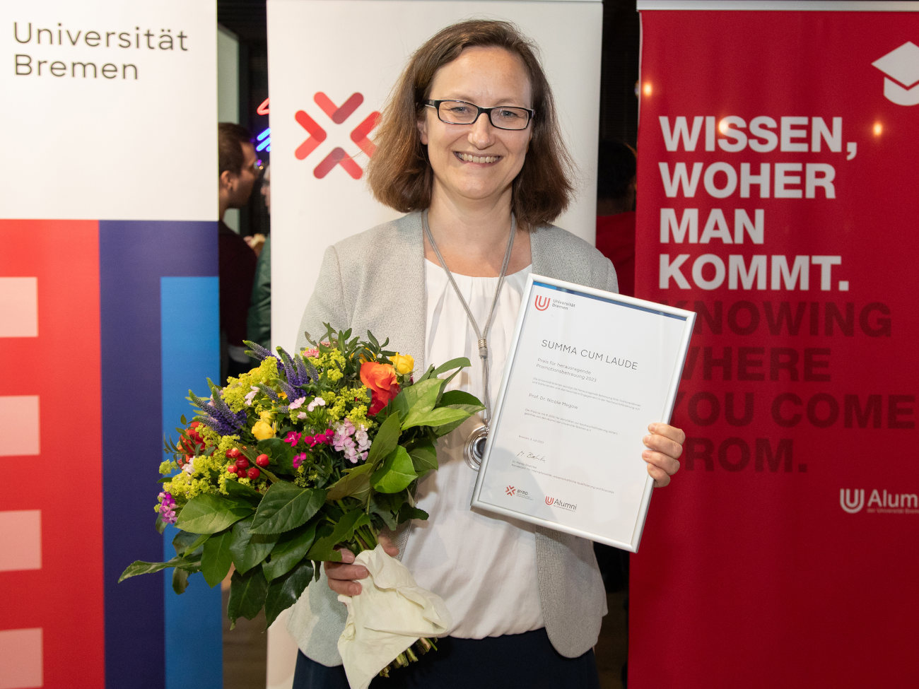 Nicole Megow with a bouquet of flowers in one hand and the certificate for outstanding doctoral supervision in the other.
