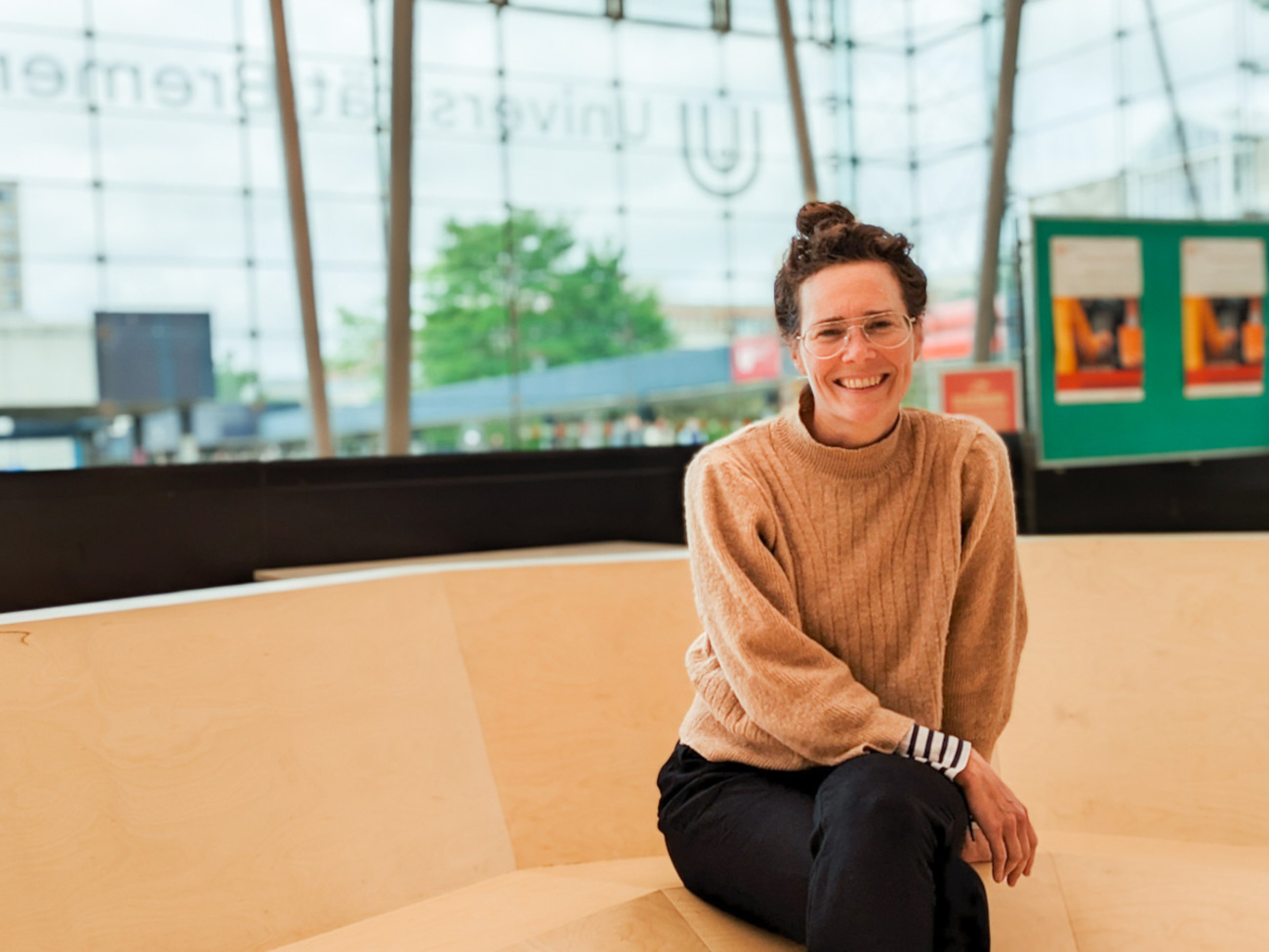 Zu sehen ist die Künstlerin Sarah Lüdemann. Sie sitzt auf dem Kunstwerk “Sitznest” in der Glashalle der Universität Bremen.
