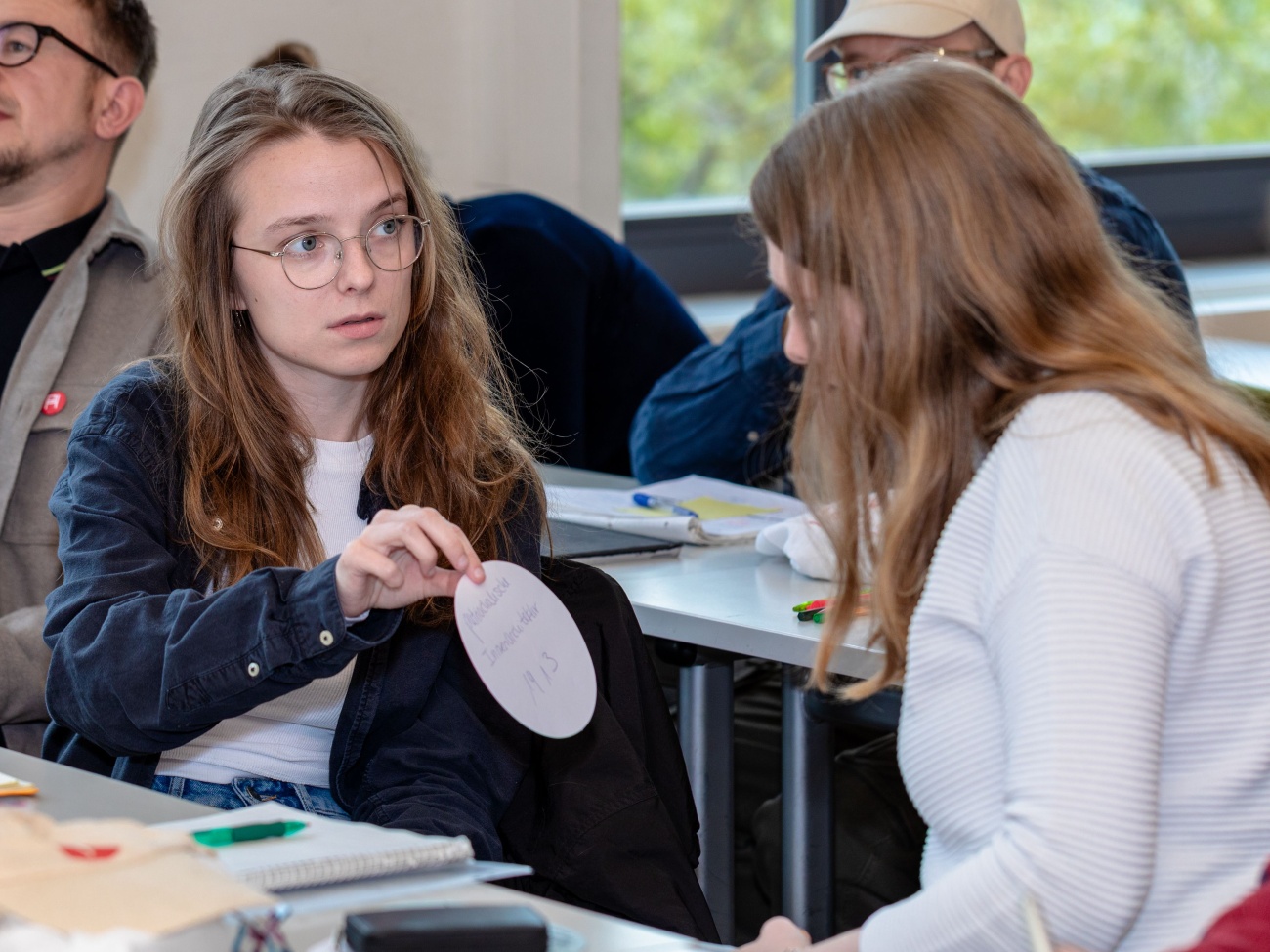 Zwei Studierende sitzen an einem TIsch und tauschen sich über ein Thema aus, das auf einer Karte steht.