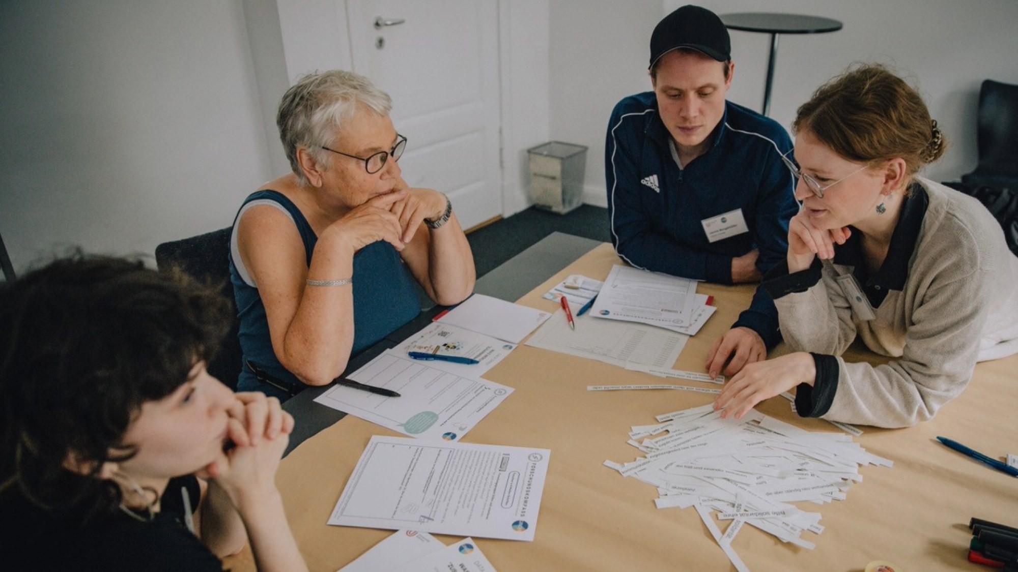 Three people sitting together at a table and talking about the papers on the table.