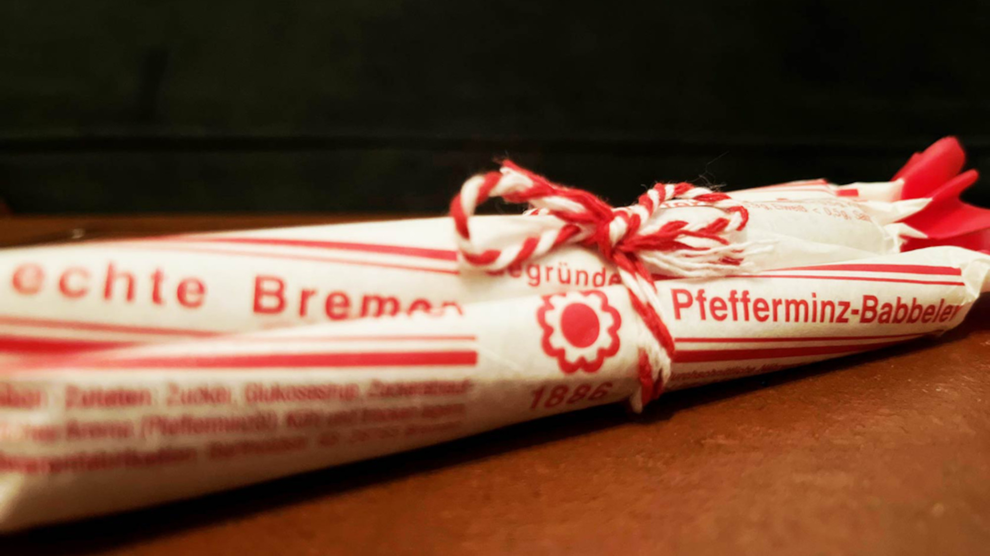 Five wrapped peppermint sticks in red and white paper sit on a table