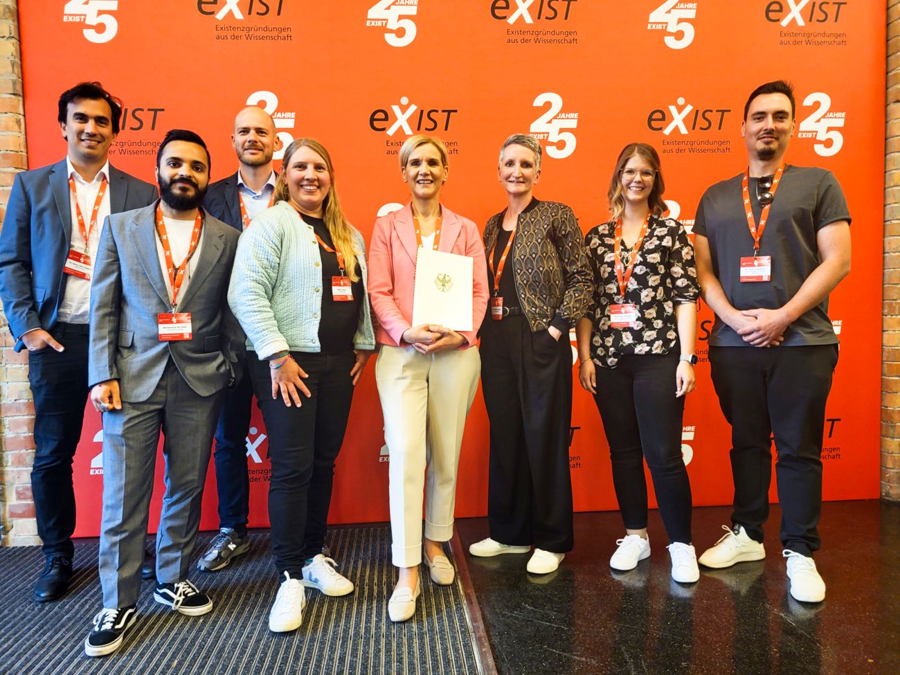 Dr. Daniel Otero Baguer (aisencia GmbH), Ali Alam (Constructor University), Ole Bast (Officer for Start-ups and Cultural and Creative Industries, Bremen), Meike Goos, President Professor Jutta Günther, Anne-Kathrin Guder (University of Bremen), Franziska Gloeden, and Dr. Tino Uhlendorf (University of Oldenburg) (from left to right) are standing in front of a banner saying “exist.”