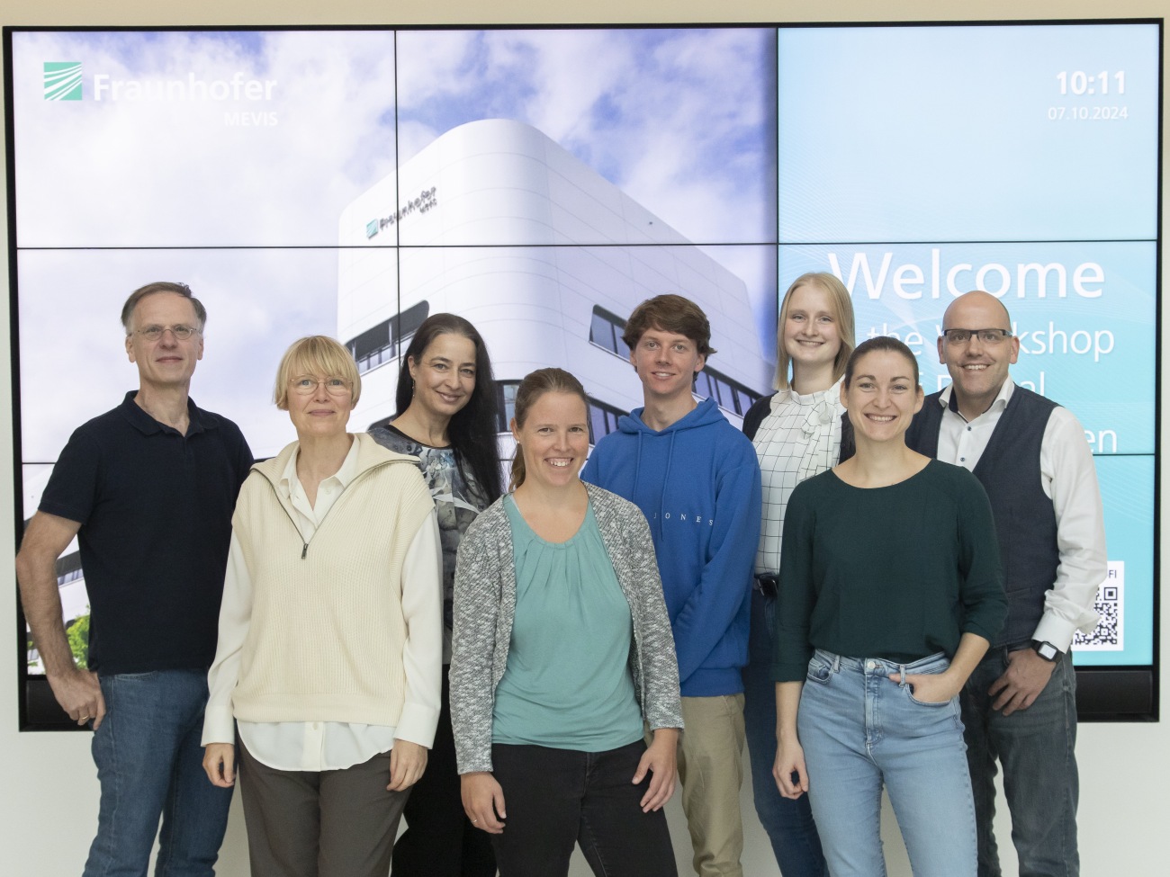 Ein Team von acht Personen steht vor einem großen Flachbildschirm.