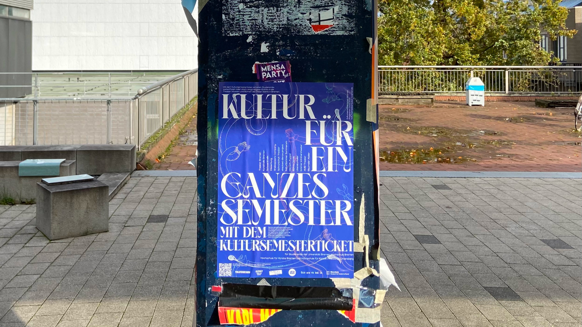 On a pillar at the university boulevard hangs a blue poster with information on the Kultursemesterticket.