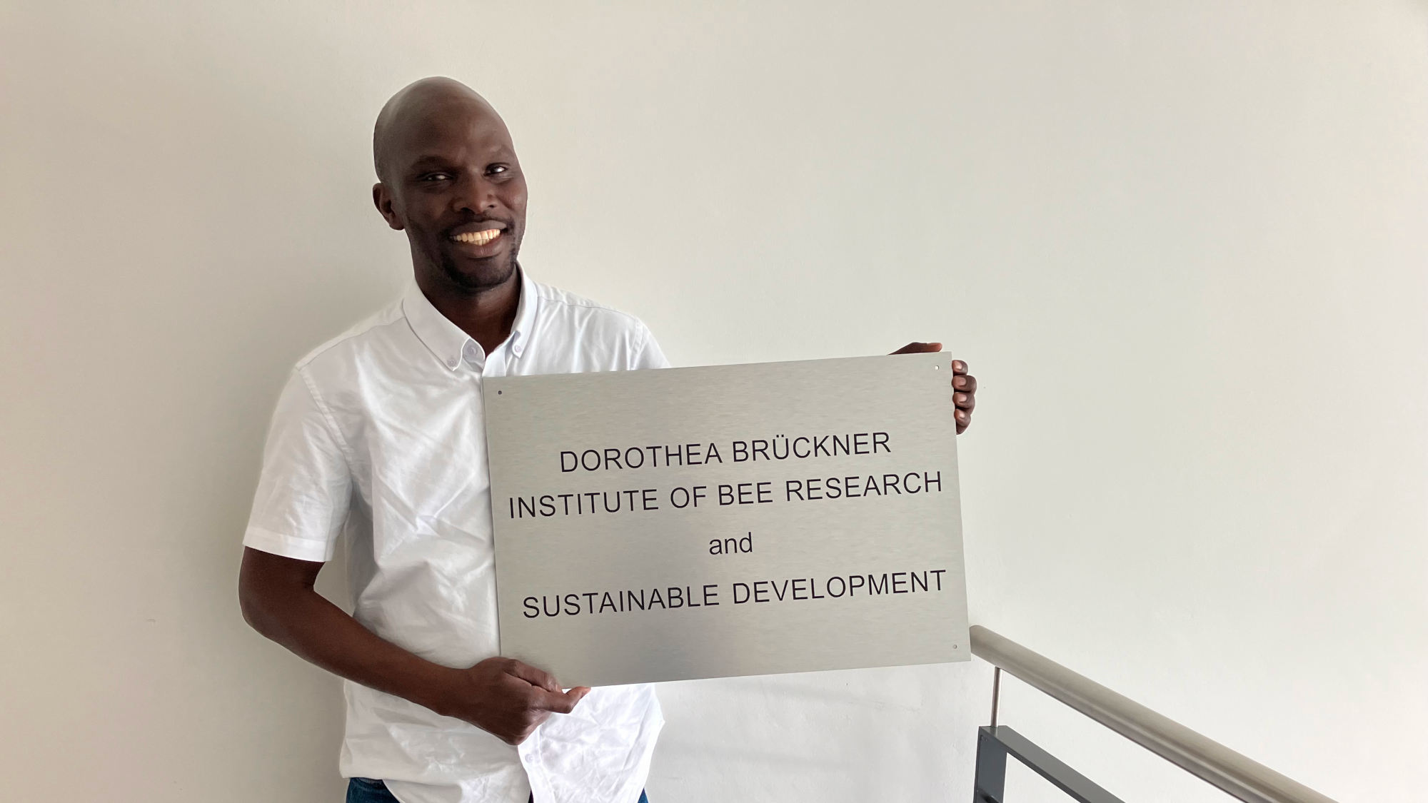 Mazi Sanda is holding a sign that reads “Dorothea Brückner Institute of Bee Research and sustainable development”. 