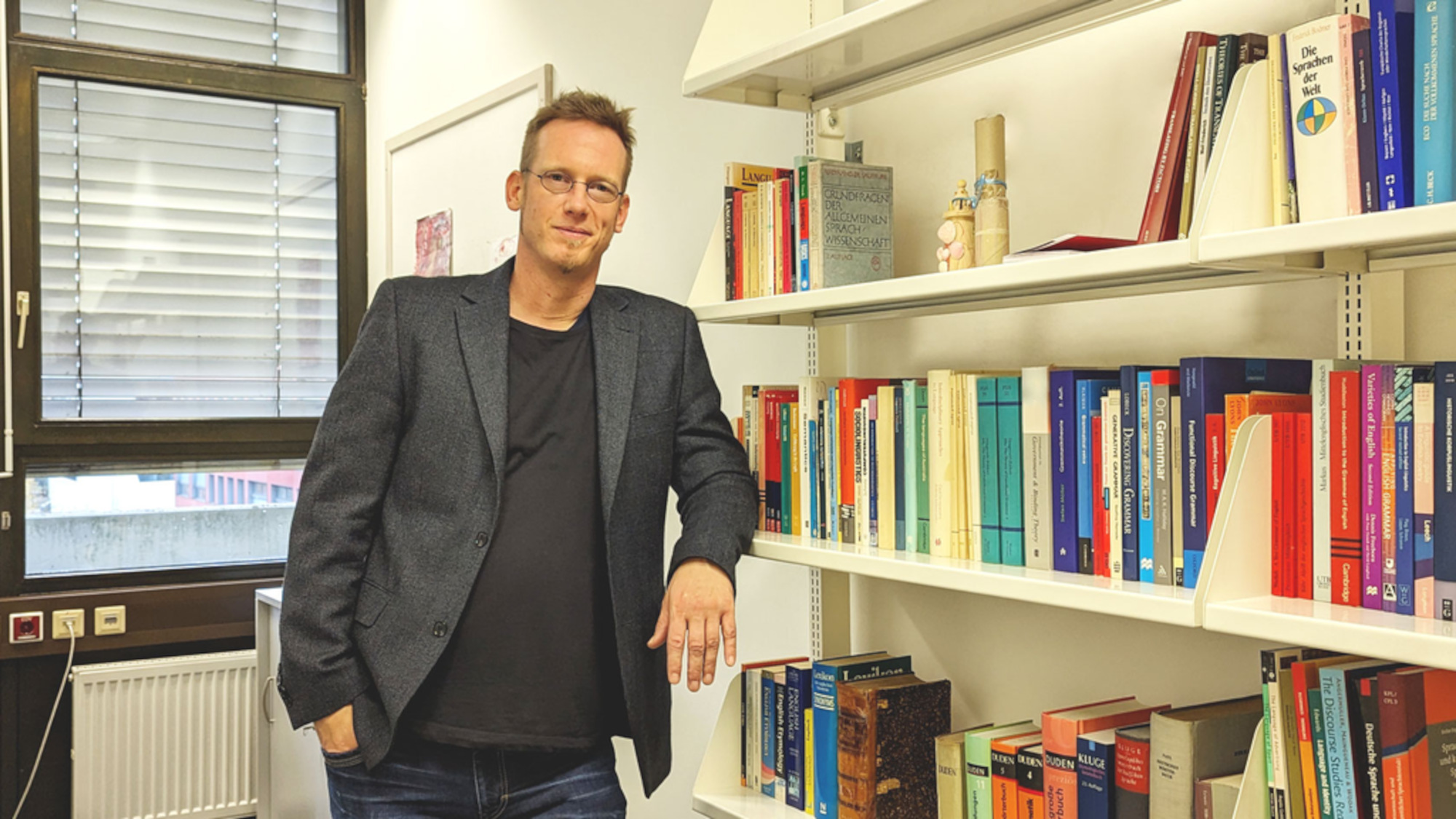 Andreas Jäger stands next to a bookshelf in his office.