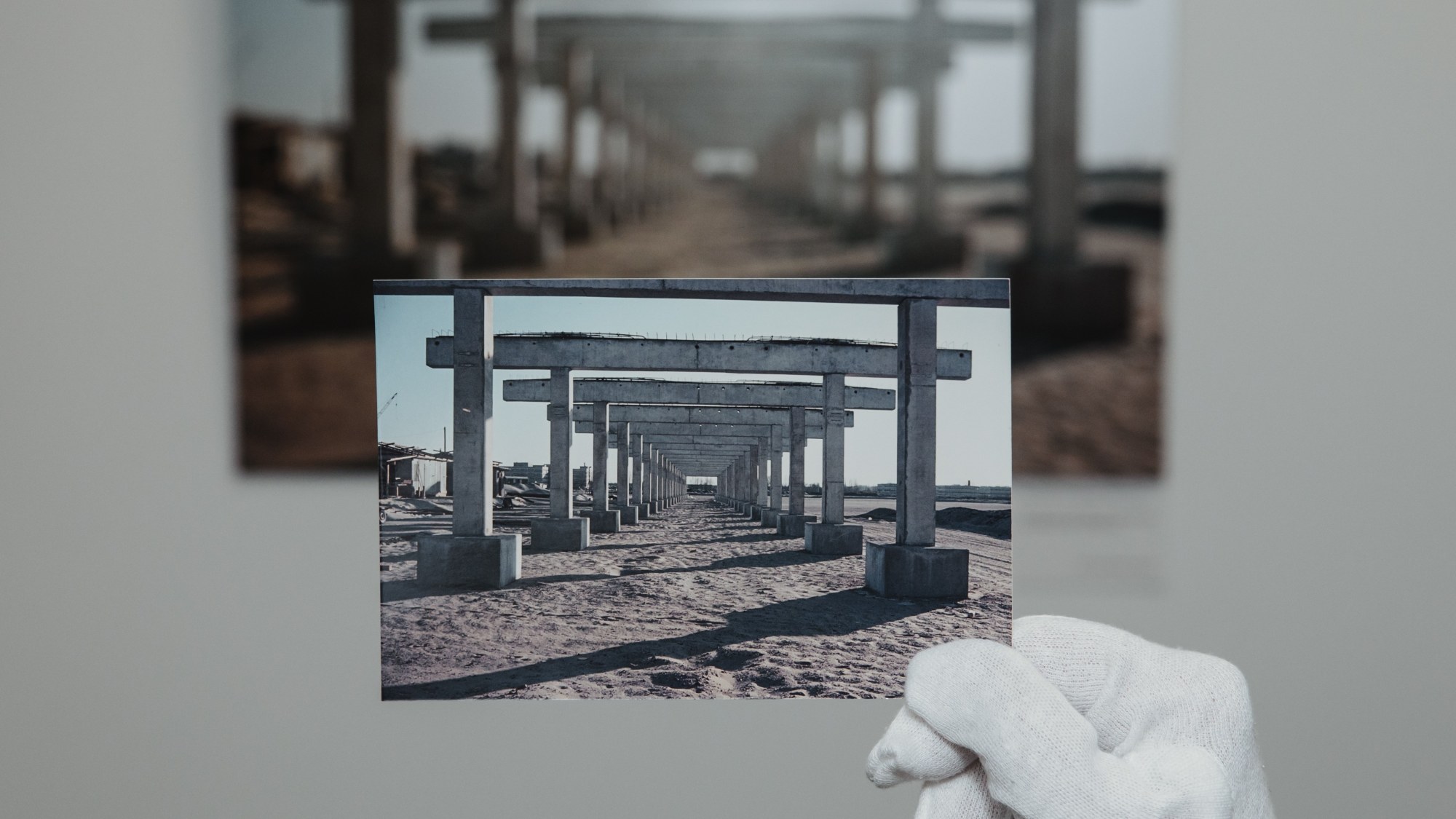 A hand in a white glove holds one picture in front of another.