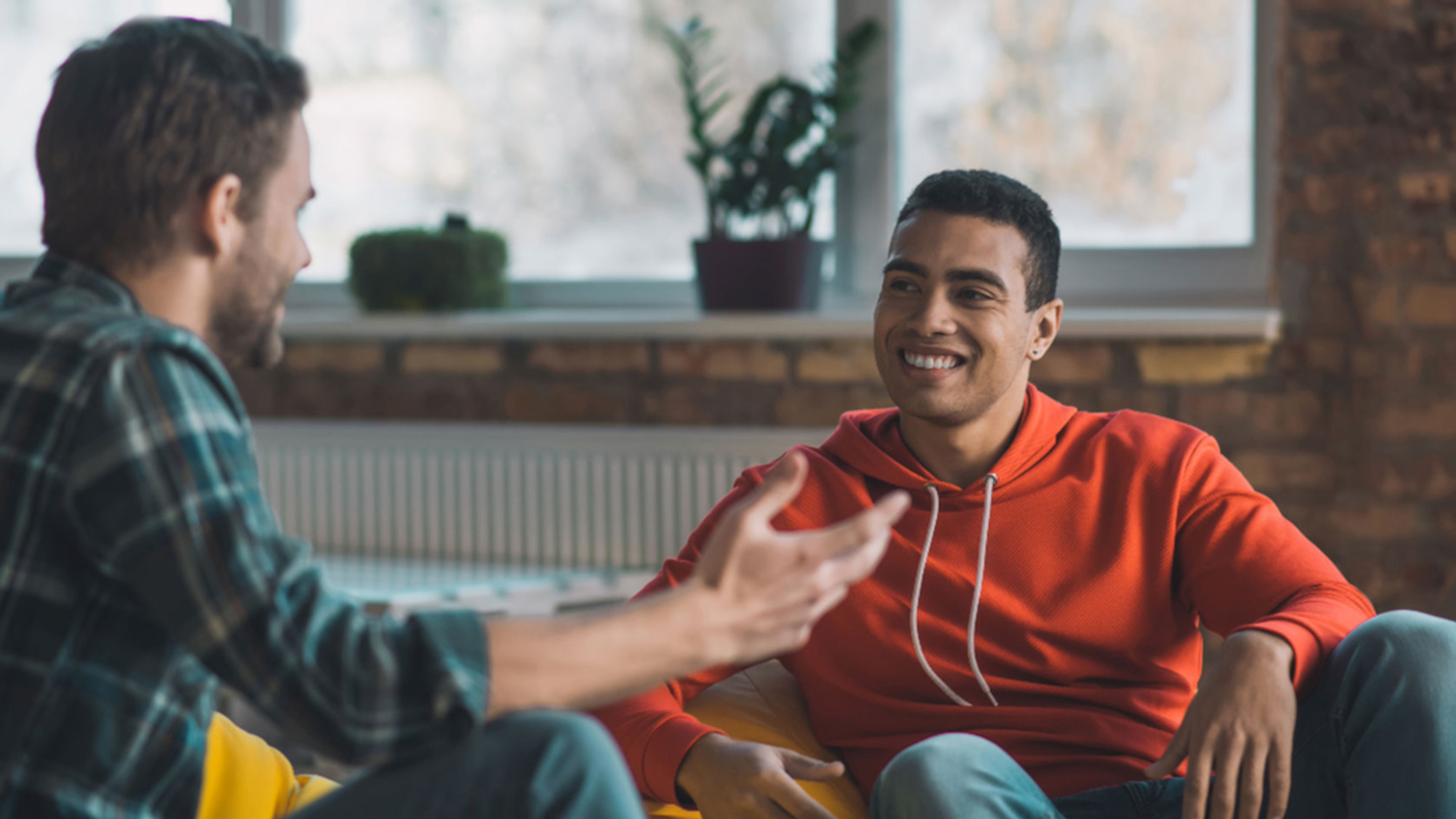 Zwei junge Männer sitzen im Wohnzimmer auf dem Sofa und unterhalten sich