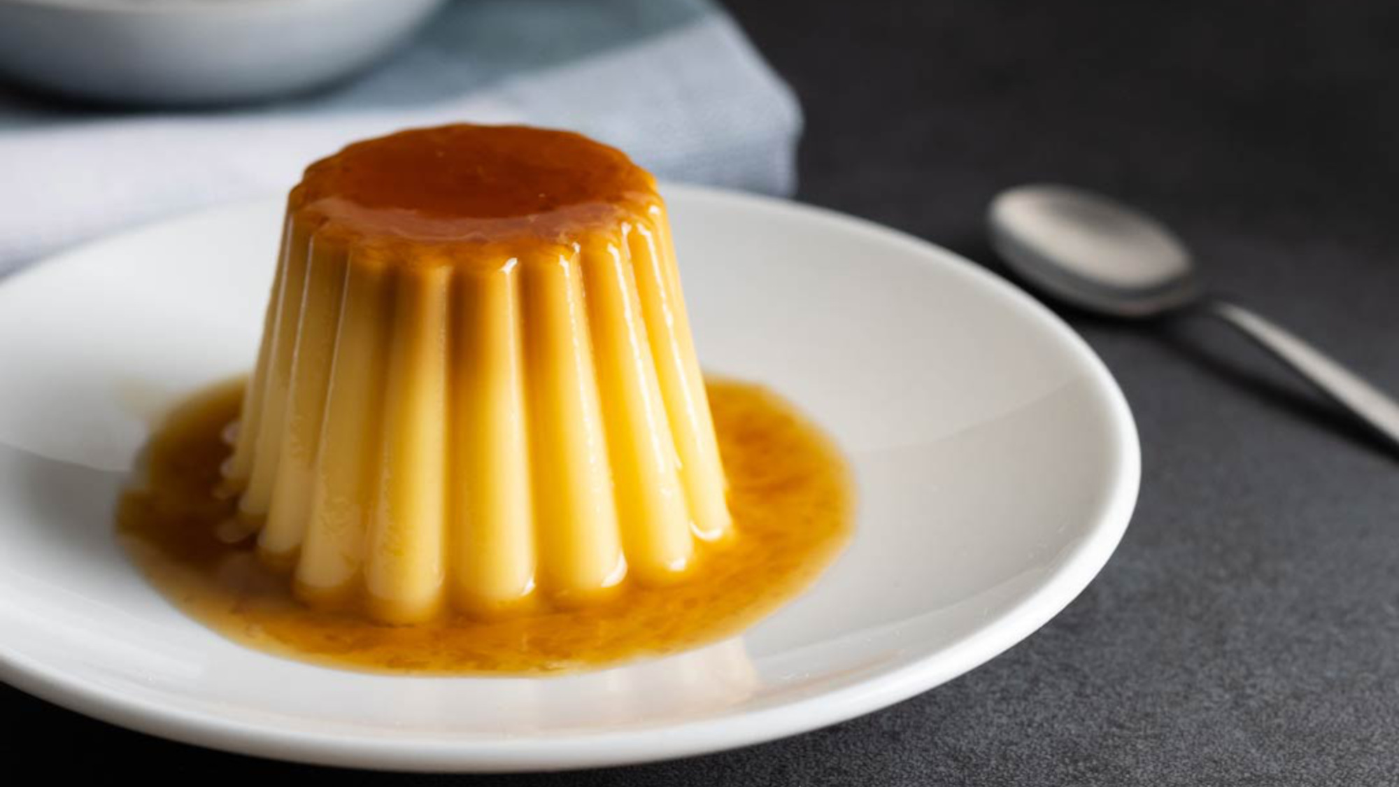 A small vanilla pudding sits on a plate and is covered with caramel sauce